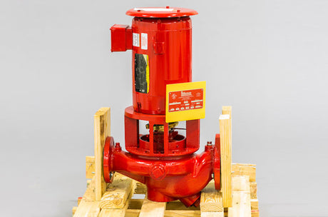 A red industrial pump on a wooden pallet, featuring a cylindrical top and wide base, set against a neutral background.