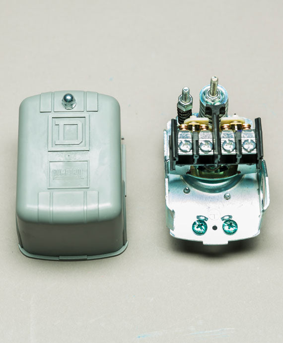 A SQUARE D Pressure Switch (30-50 PSI, 1/4" Female Single Port, DPDT, 10A) in gray metal is shown with the cover removed for inspection. Screws and terminals for water pump use are exposed against a plain background. Cover contrasts on the left.