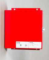 A red electrical enclosure by Eaton, featuring a Life Safety Panel, is mounted on the wall. The enclosure includes a metal latch on the right side and prominently displays labels with technical specifications on the front.